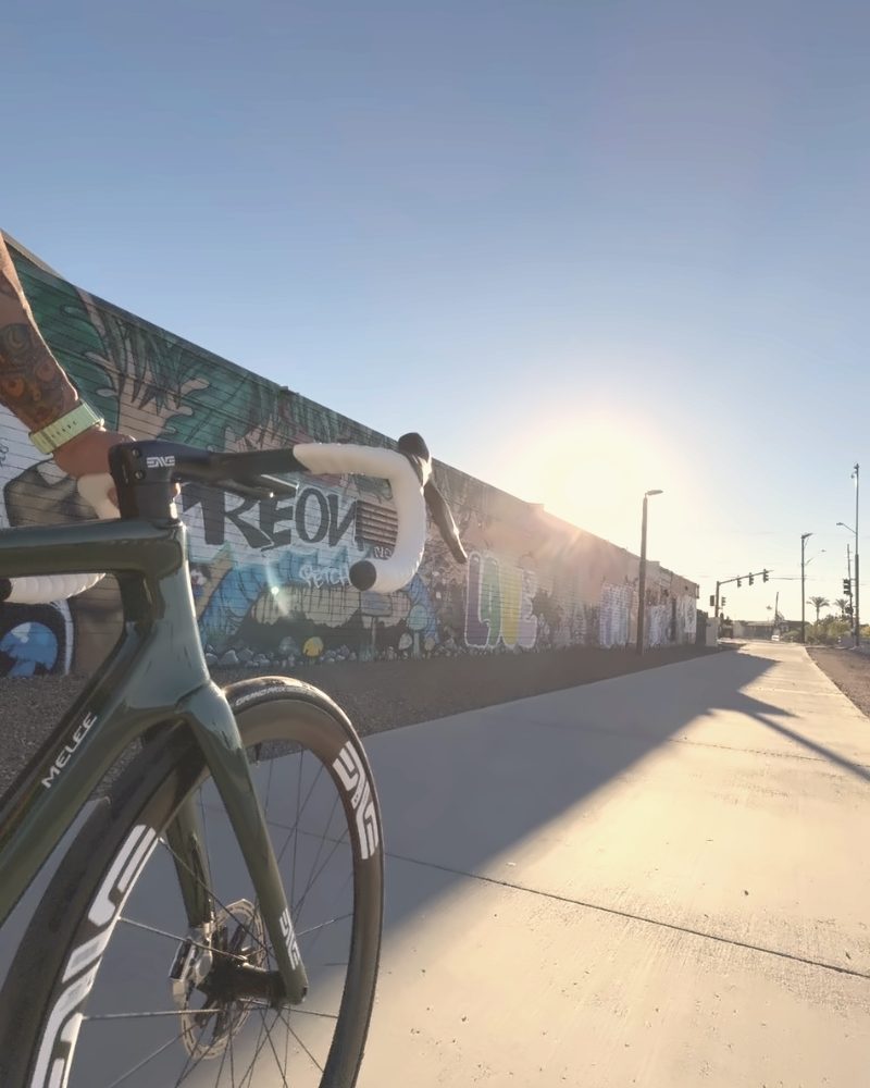 A bike leaned on a painted wall, low sun down the street.