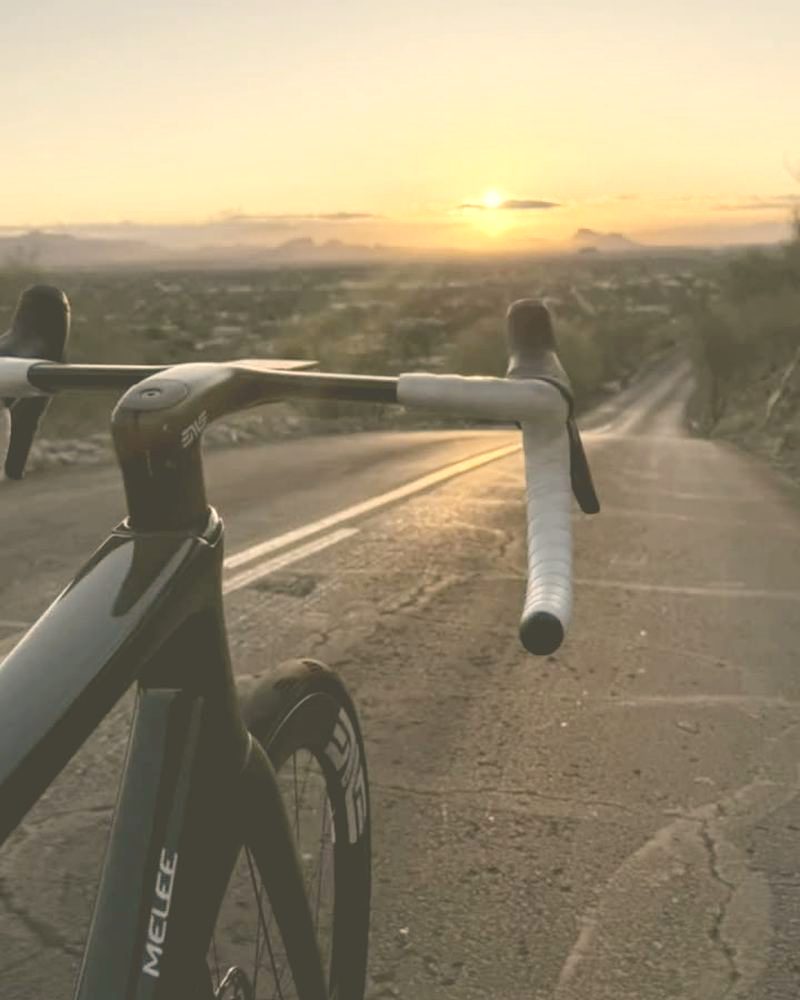 Handlebars pointed down a mountain road at sunset, the valley lit below.