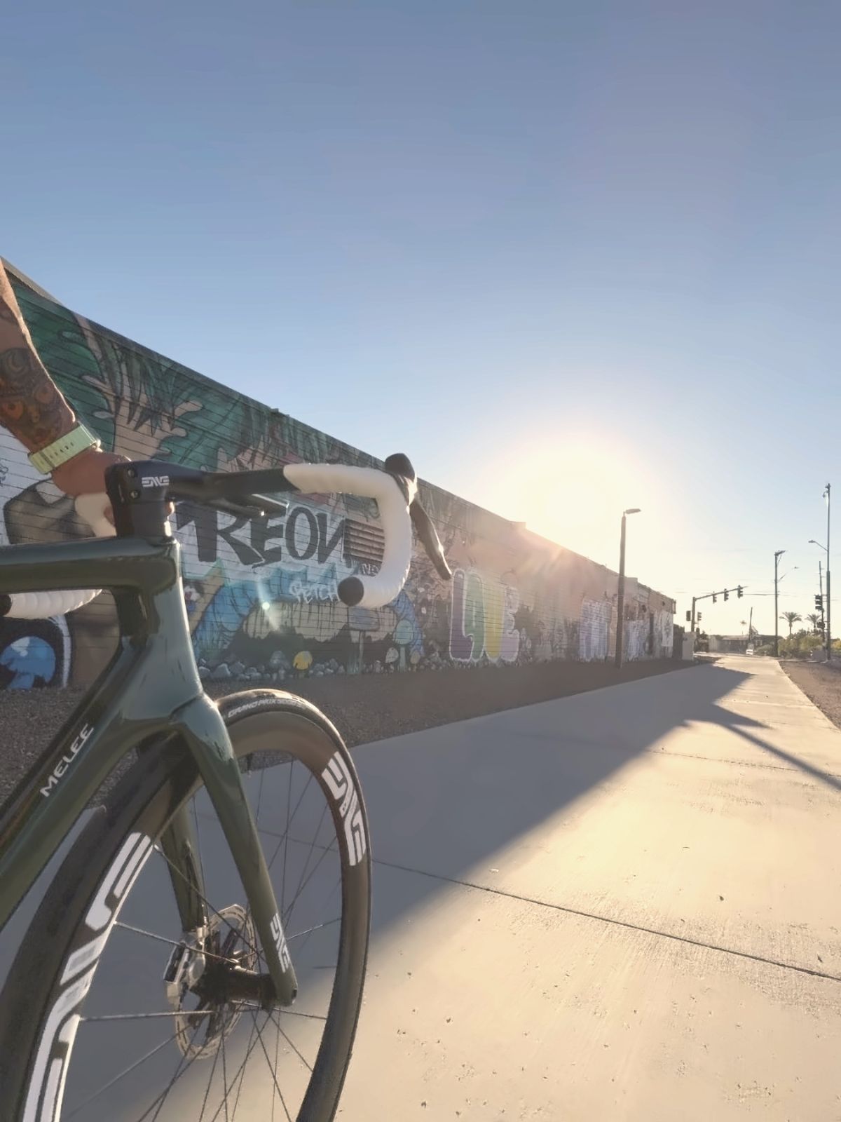 A bike leaned on a painted wall, low sun down the street.