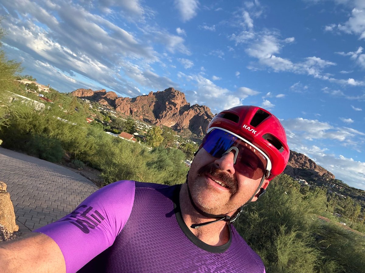 Robert mid-ride in a red helmet and a purple jersey, Camelback Mountain behind him.