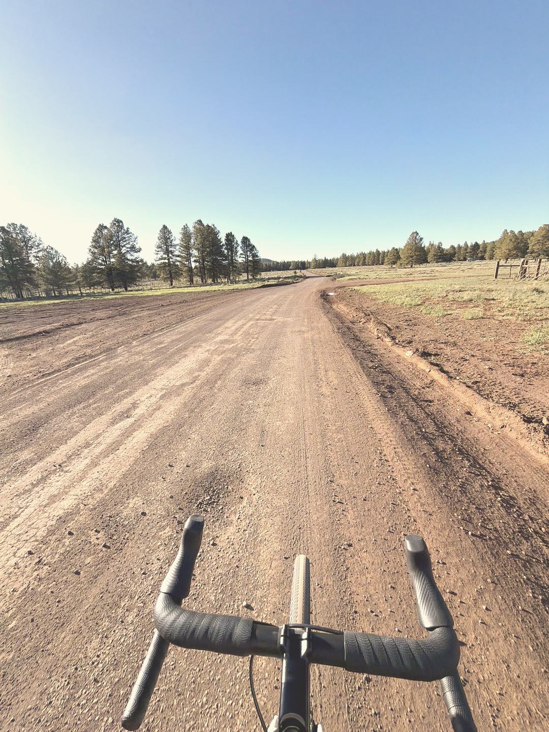 A wide, rutted dirt road under a big sky, seen over the handlebars.