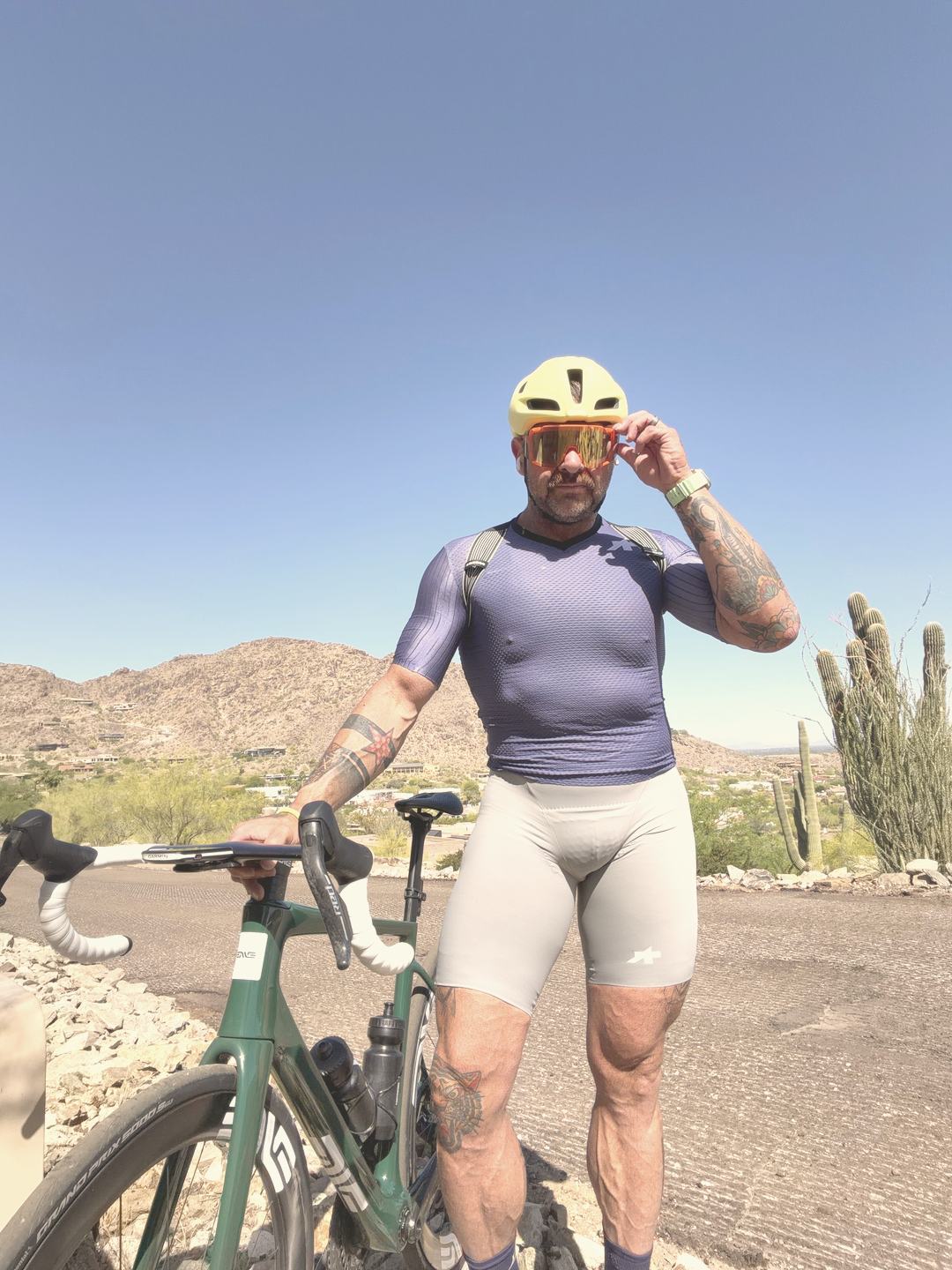 Robert standing with his bike on a desert overlook in a yellow helmet, saguaros behind him.